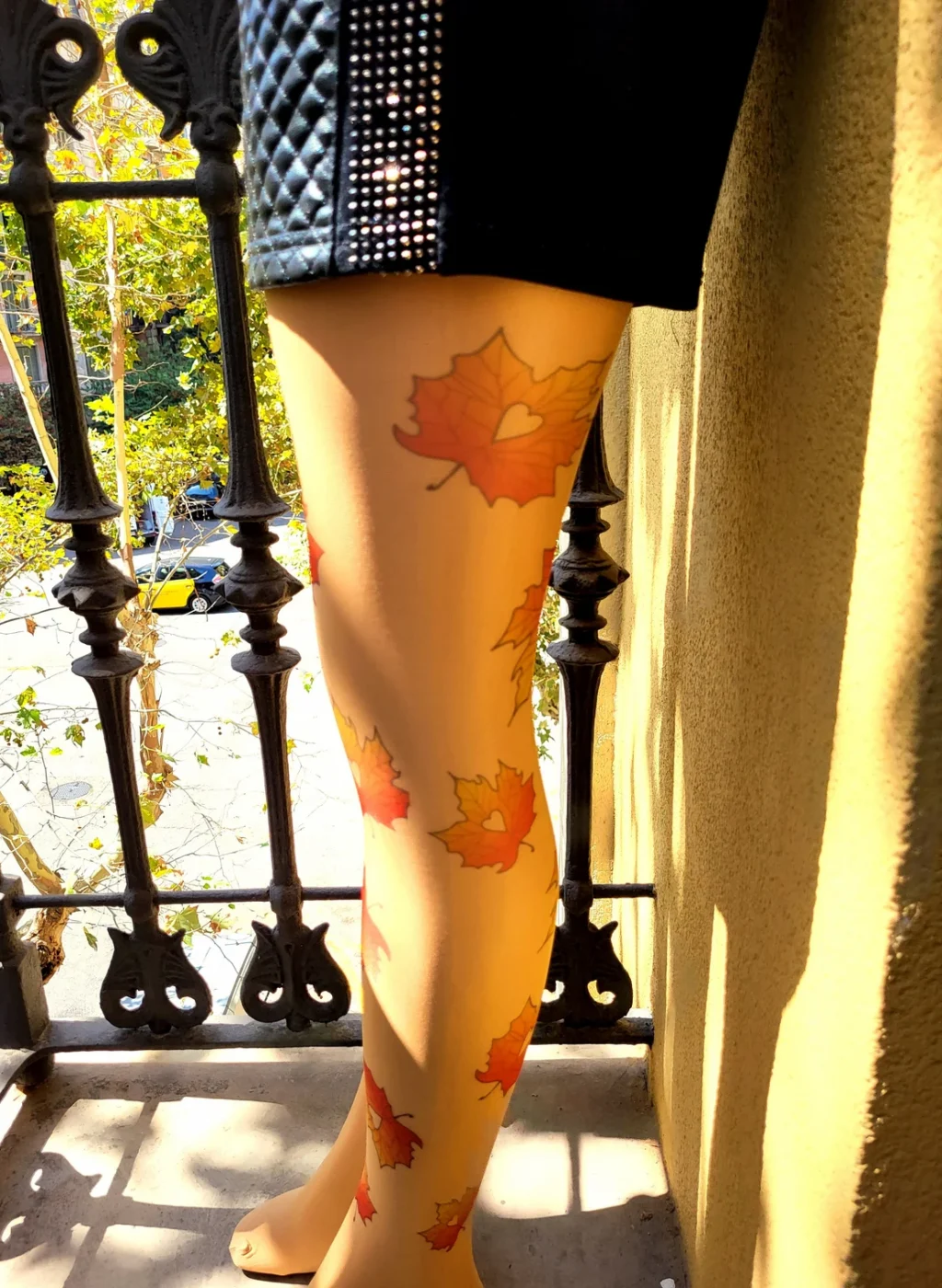 Pantimedias beige con hojas de otoño al sol en un pasillo exterior junto a barandilla de hierro | Beige tights with autumn leaves print in outdoor hallway beside iron railing