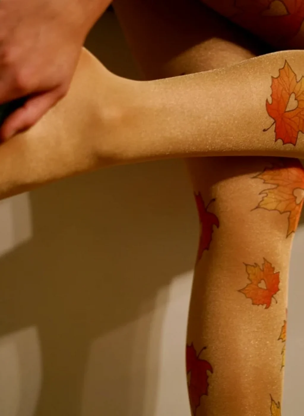 Pantimedias beige con estampado de hojas de otoño mientras una mujer se ajusta un zapato verde | Beige tights with autumn leaves print as a woman adjusts a green shoe