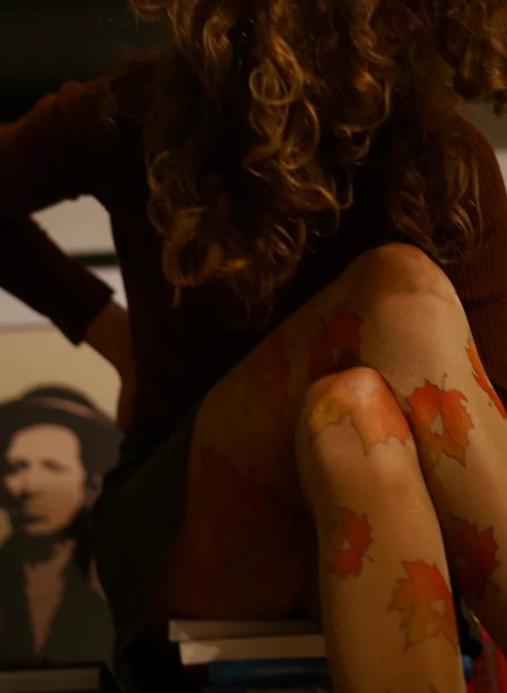 Pantimedias color piel con hojas de otoño estampadas mientras una mujer se sienta con fondo artístico | Nude tights with autumn leaves print worn by a seated woman with art background