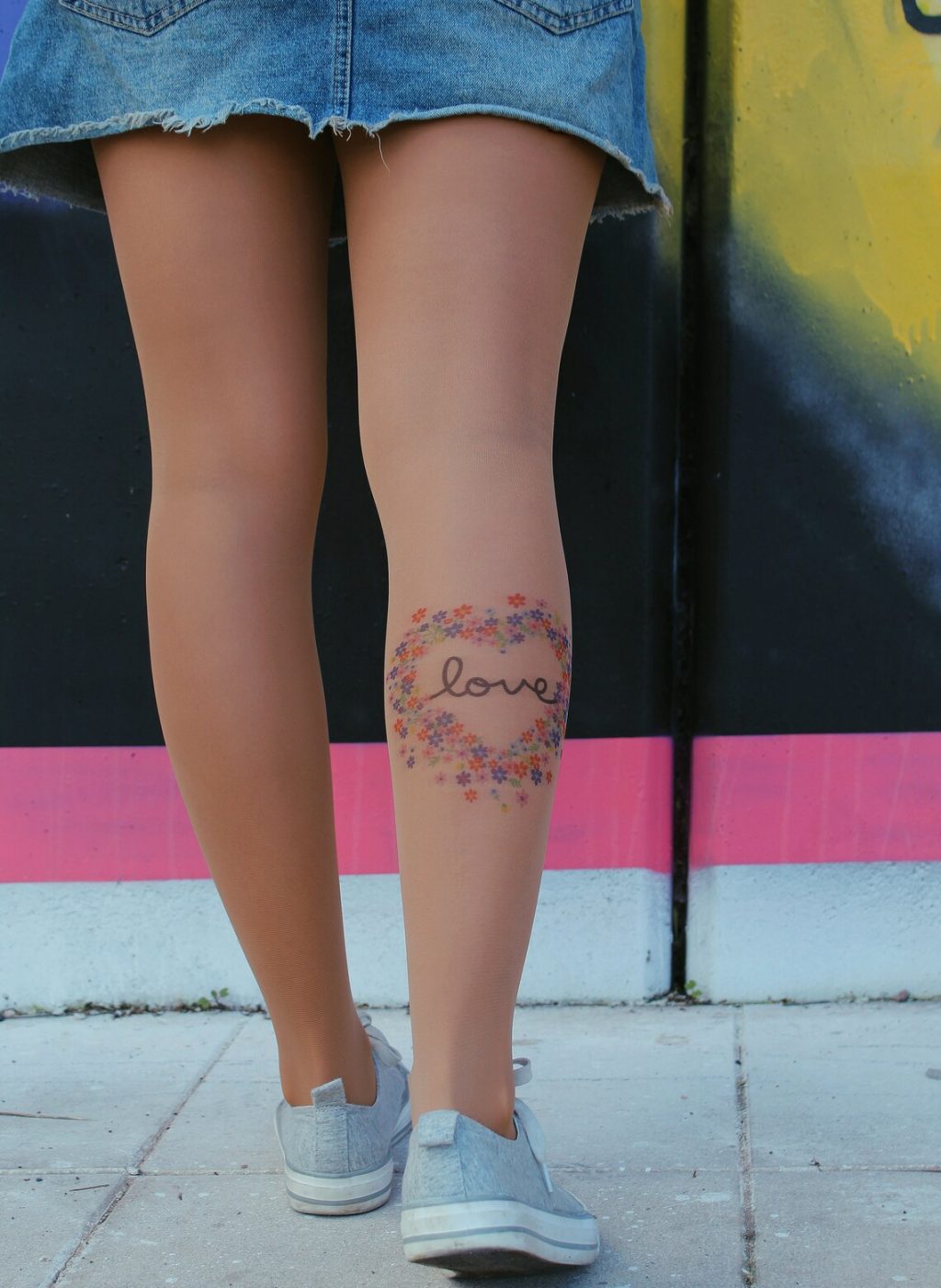 Legs wearing sheer beige pantyhose with floral heart and love design, standing outdoors with denim skirt | Piernas con pantimedias beige transparentes con diseño de corazón floral y la palabra love, en exterior con falda vaquera