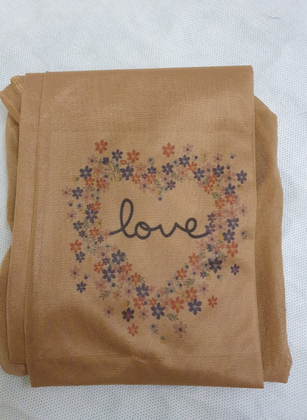 Folded sheer pantyhose in beige with floral heart design and the word love printed on the fabric | Pantimedias beige dobladas con diseño de corazón floral y la palabra love impresa en el tejido