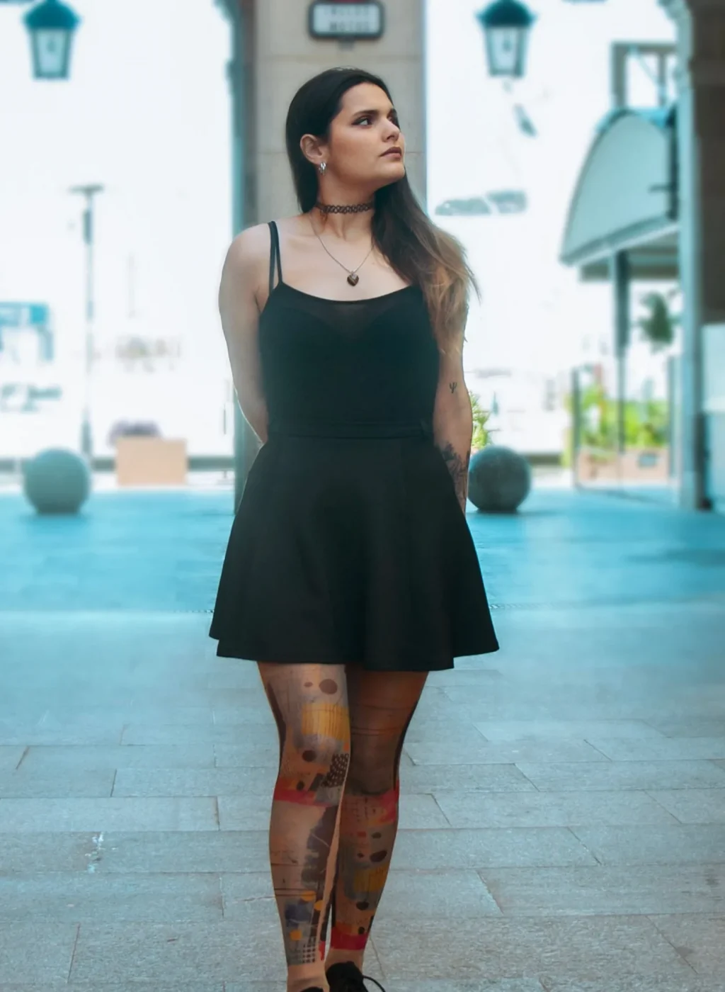 Mujer con pantimedias de arte abstracto posando de pie en entorno urbano con vestido negro | Woman wearing abstract art tights standing in urban setting with black dress