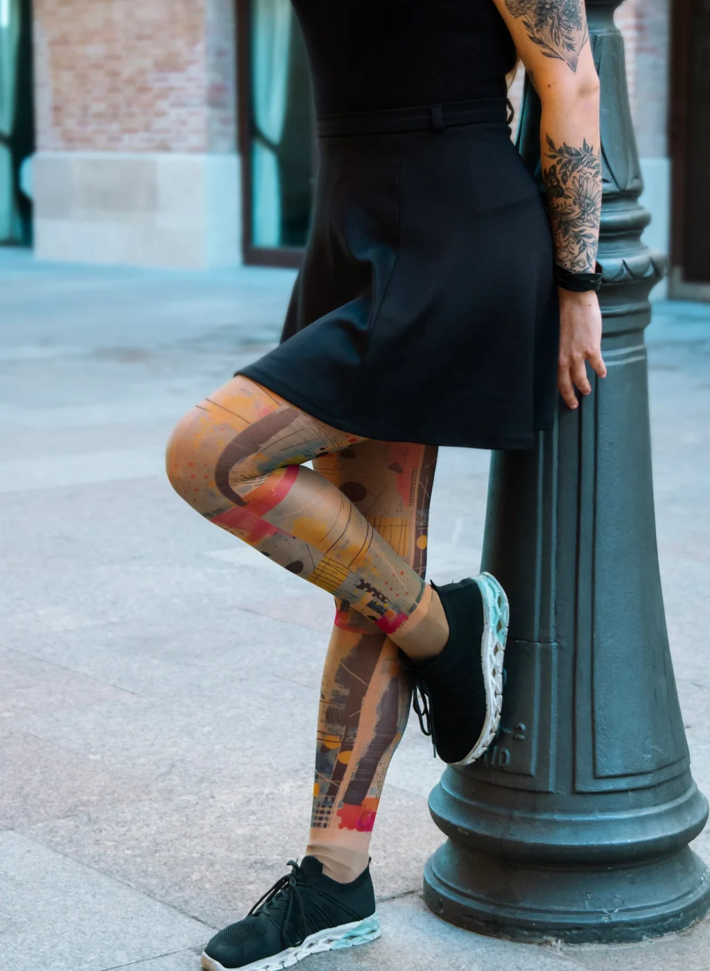 Mujer con pantimedias arte abstracto multicolor apoyada en farola urbana | Woman wearing multicolor abstract art tights leaning on street lamp