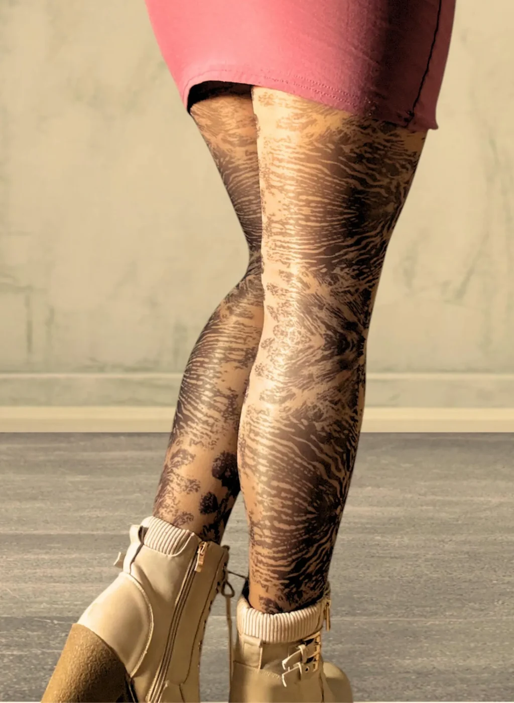 Piernas con pantimedias Wildwood en estampado negro rebajado sobre media transparente combinadas con falda rosa en fondo beige | Legs wearing Wildwood tights with muted black pattern on sheer hosiery paired with pink skirt against beige background