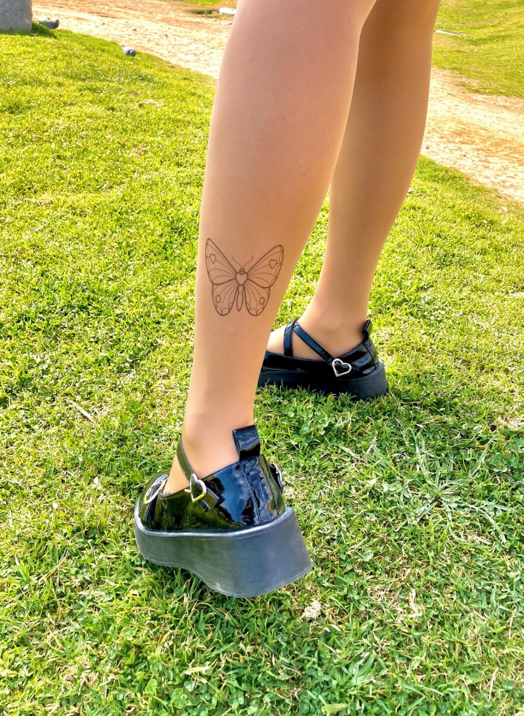 Sheer nude tattoo tights with minimalist butterfly design on the calf, outdoor grass background | Pantimedias nude semitransparentes con diseño minimalista de mariposa en el gemelo, fondo de césped exterior