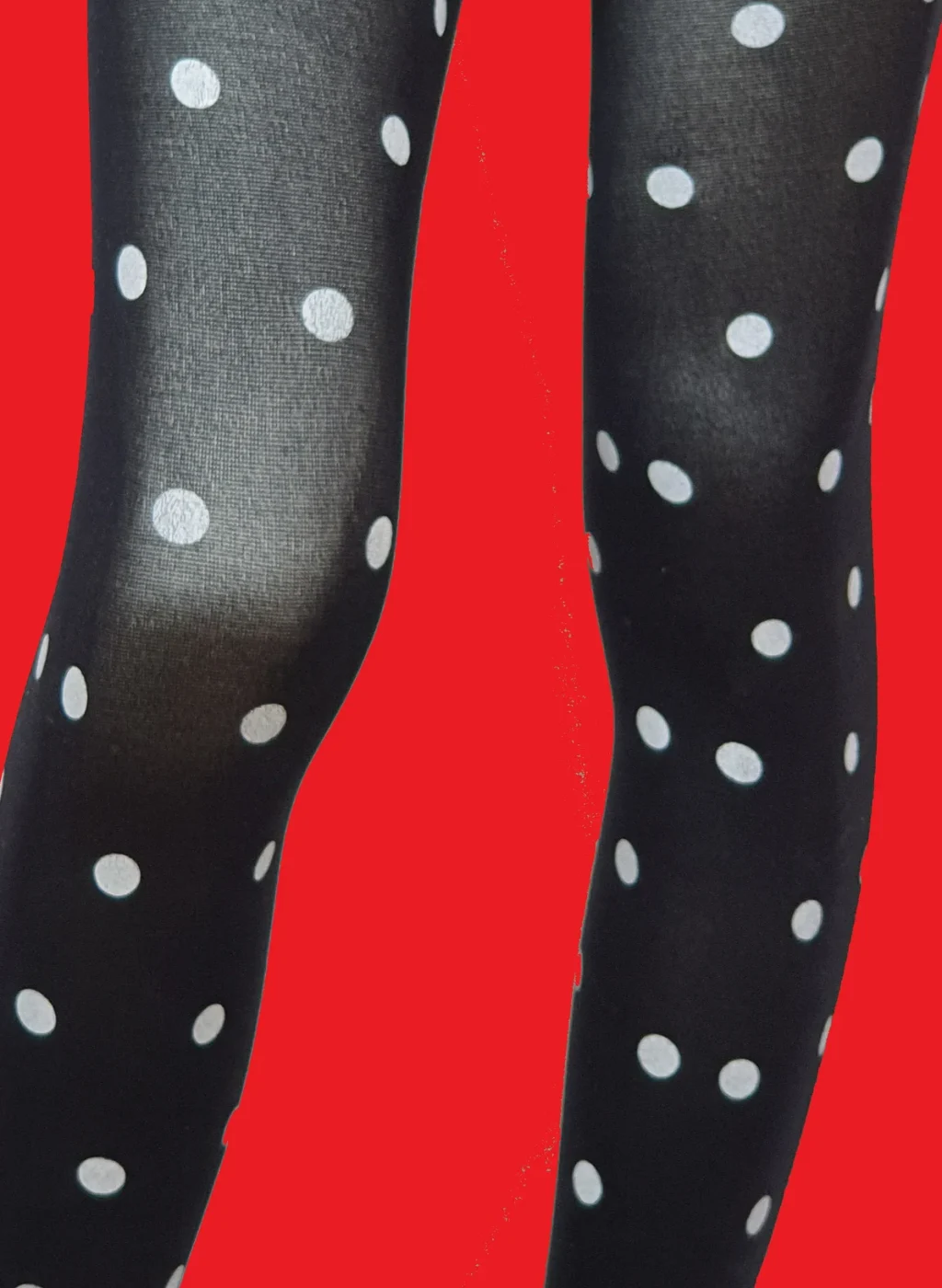 Medias negras con lunares blancos sobre fondo rojo, vista frontal de las piernas. Black polka dot tights on a red background, front view of legs.