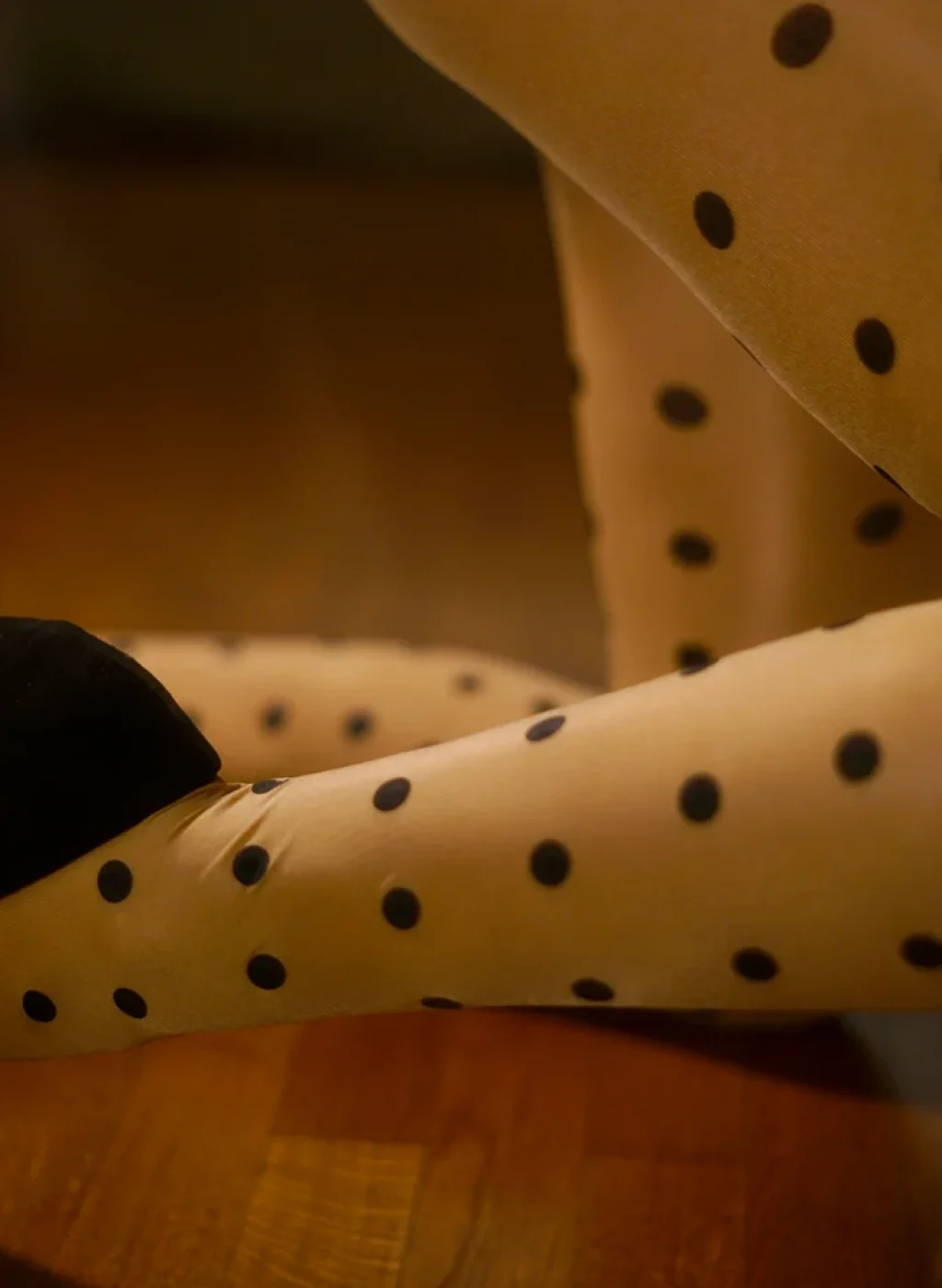 Sheer black polka dot tights with heels in elegant kneeling pose, warm ambient lighting | Pantimedias negras transparentes con lunares y tacones en pose arrodillada elegante, iluminación cálida
