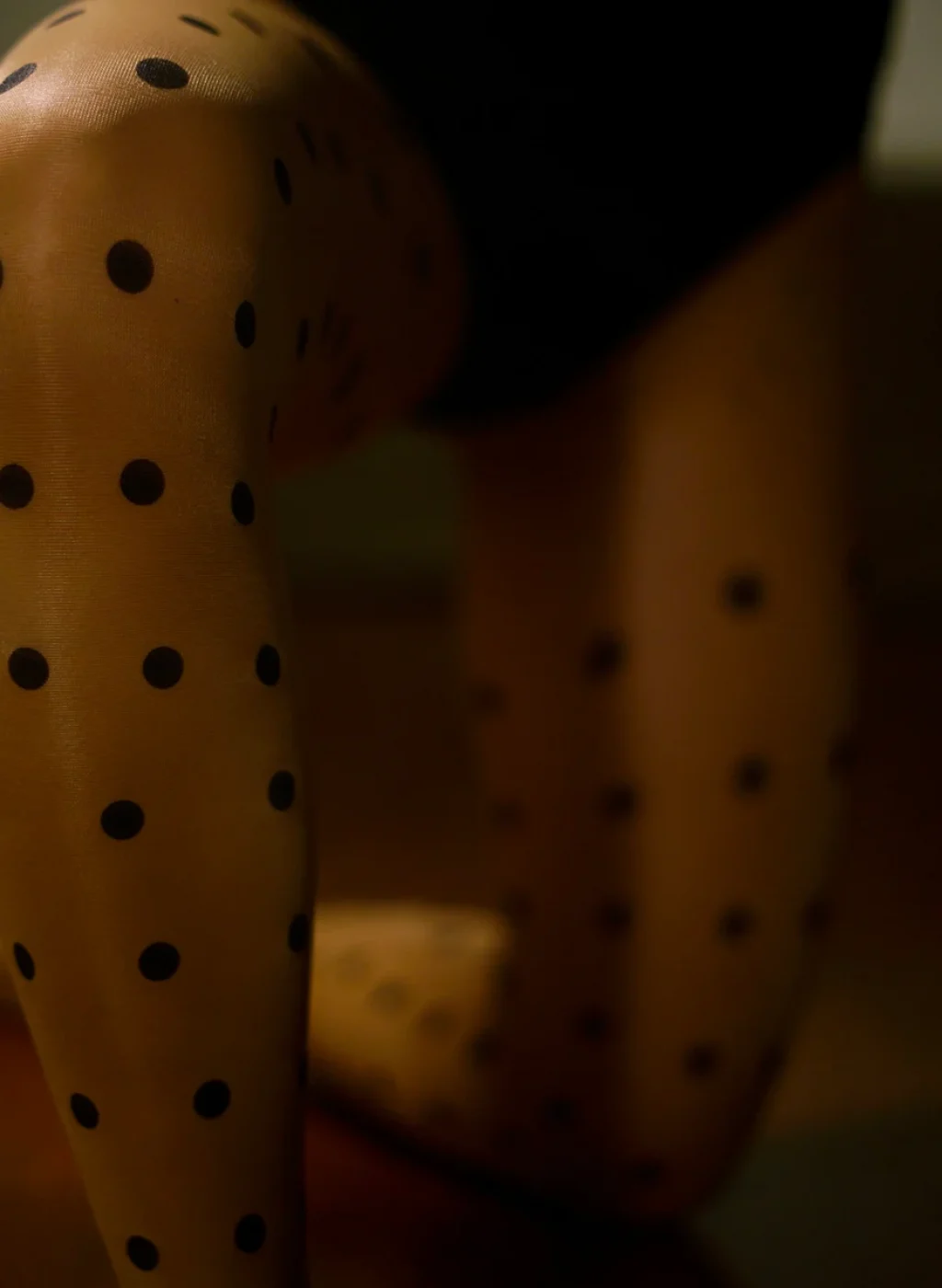 Sheer black polka dot tights close-up in soft kneeling pose, subtle texture and elegant fit | Pantimedias negras transparentes con lunares en pose arrodillada, detalle sutil y ajuste elegante