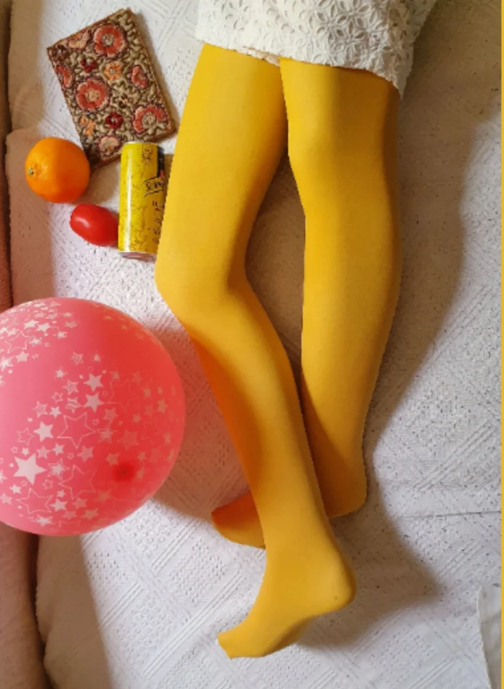 Piernas con pantimedias color mostaza posando sobre cama con fondo amarillo y objetos decorativos | Legs wearing mustard tights lying on a bed with yellow background and decorative items