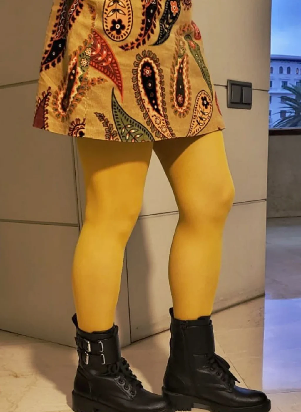 Piernas con pantimedias color mostaza combinadas con botines negros y falda estampada | Legs wearing mustard tights styled with black boots and a patterned skirt