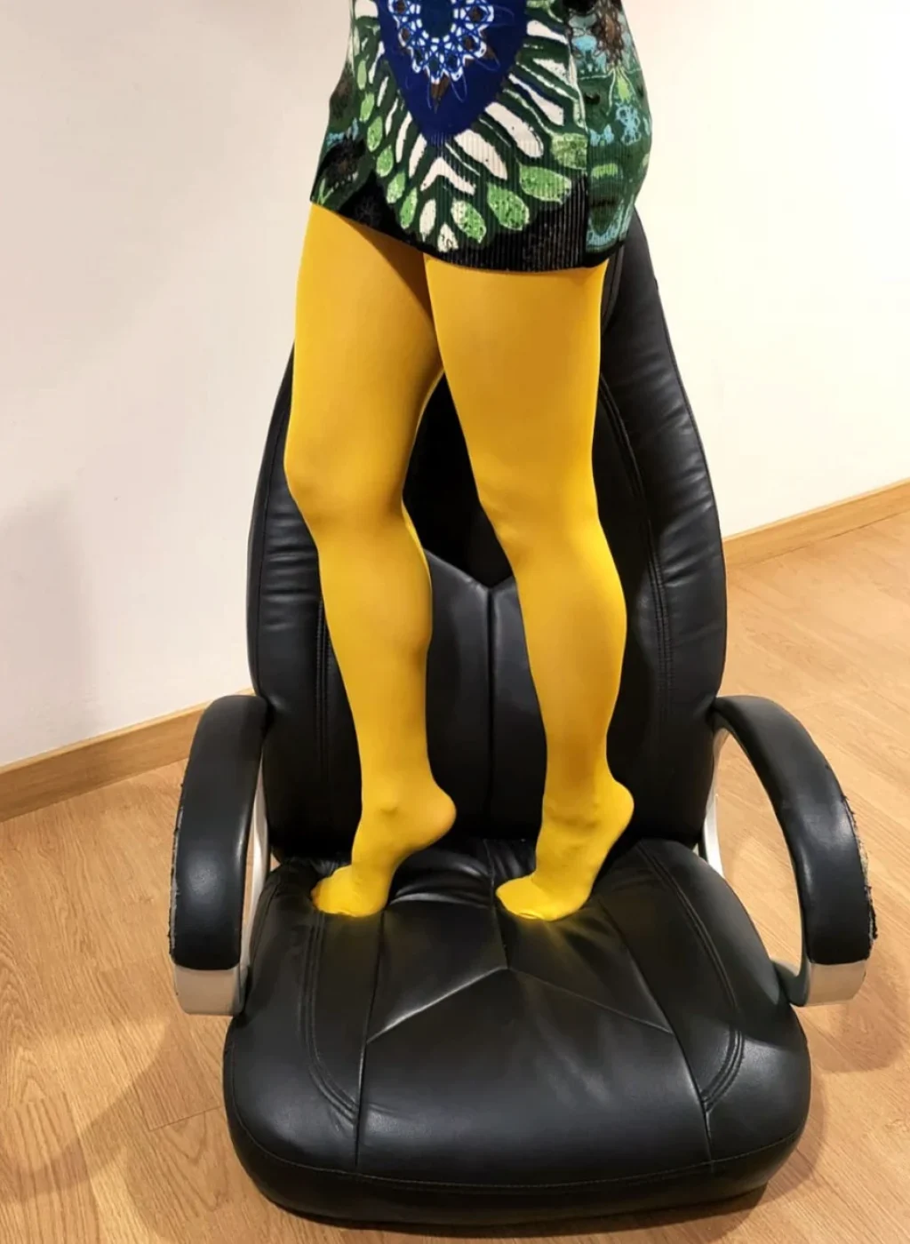 Piernas con pantimedias color mostaza posando sobre una silla negra, combinadas con falda estampada | Legs wearing mustard tights posing on a black chair with a patterned skirt