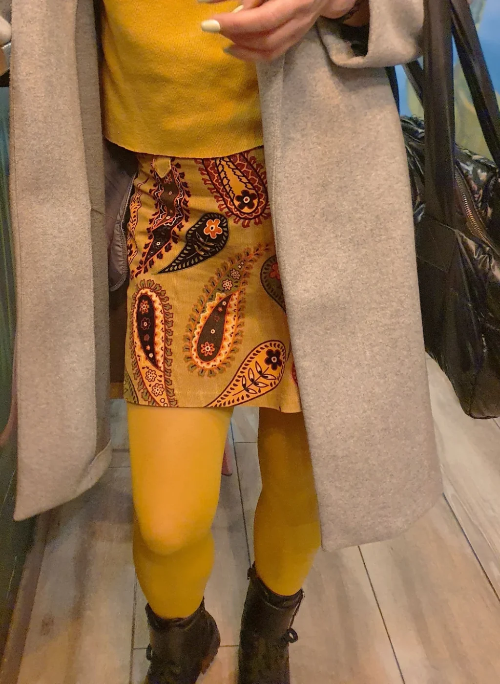 Piernas con pantimedias color mostaza combinadas con falda estampada y abrigo gris | Legs wearing mustard tights paired with a patterned skirt and grey coat