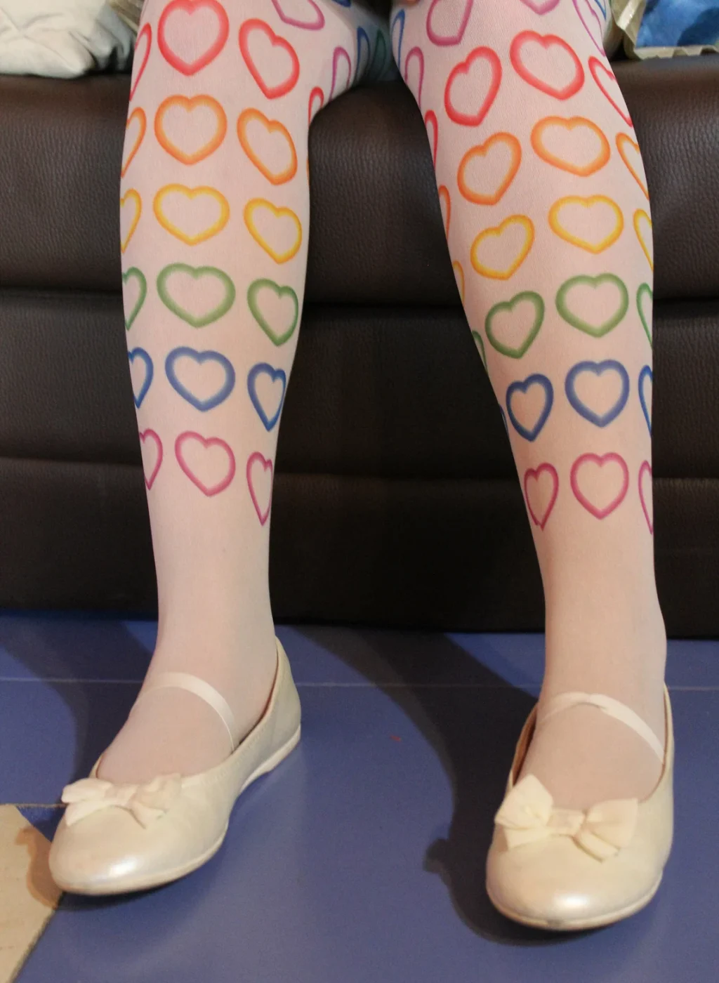 Pantimedias infantiles blancas con corazones arcoíris mientras la niña está sentada | Kids white tights with rainbow heart pattern while seated