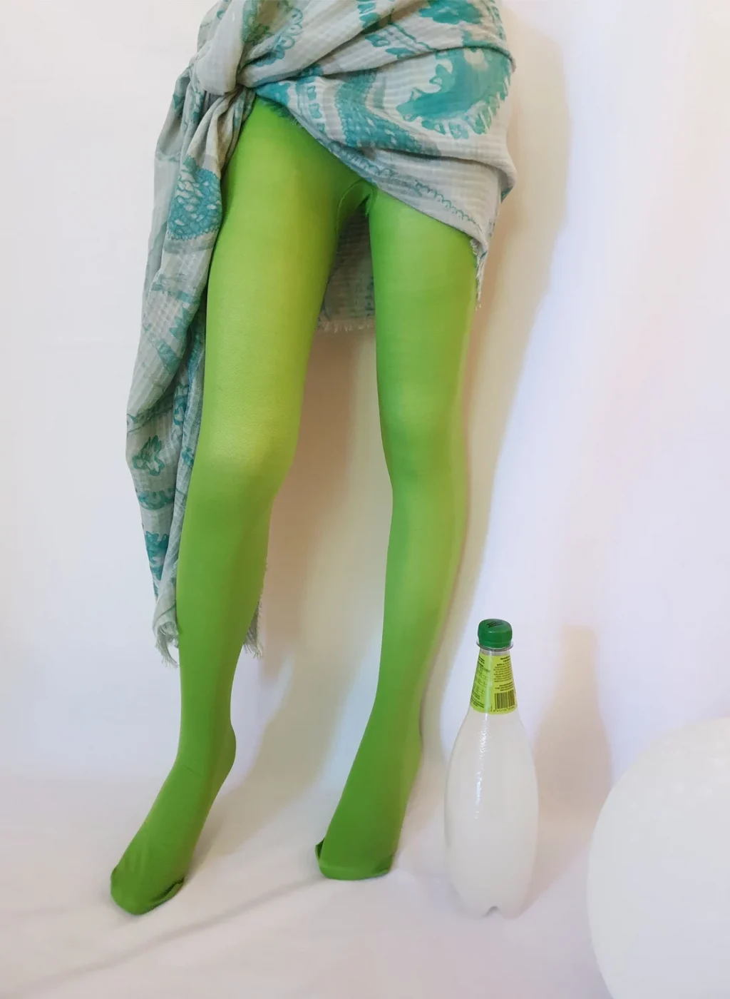 Pantimedias verde manzana en piernas de mujer con botella decorativa sobre fondo blanco | Apple green tights on woman's legs with decorative bottle on white background