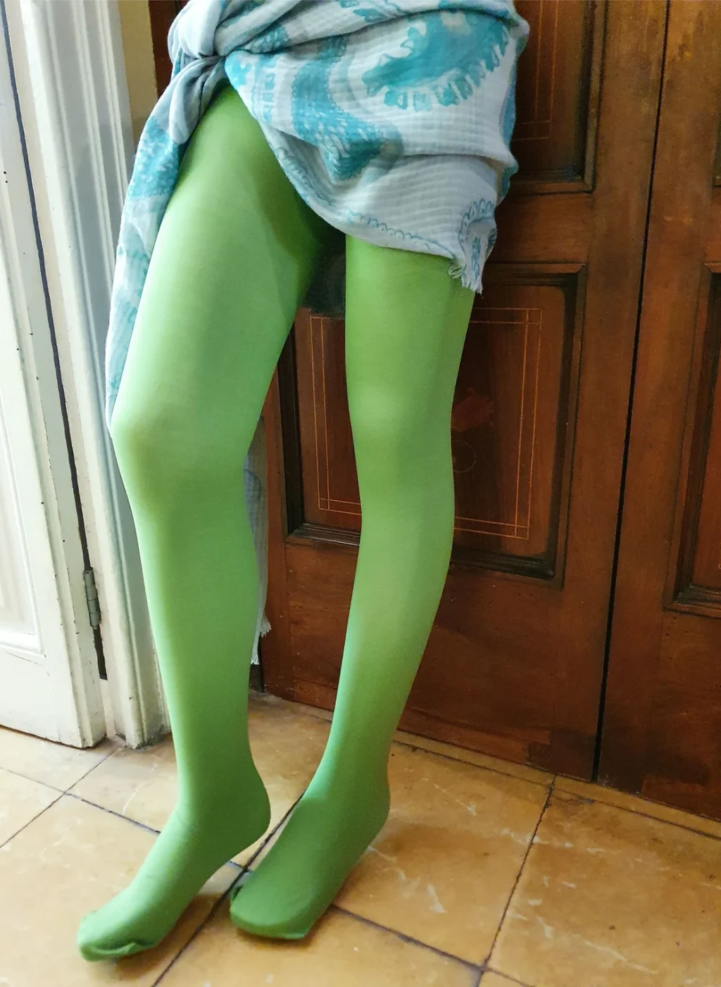 Pantimedias verdes color manzana en piernas cruzadas frente a puerta de madera | Apple green tights on crossed legs in front of wooden door